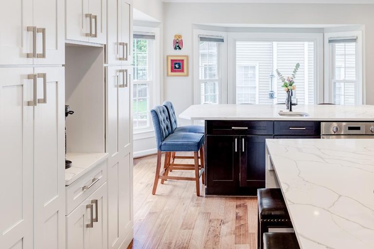 Modern kitchen with white cabinetry, dark island, blue chairs, hardwood floors and large windows