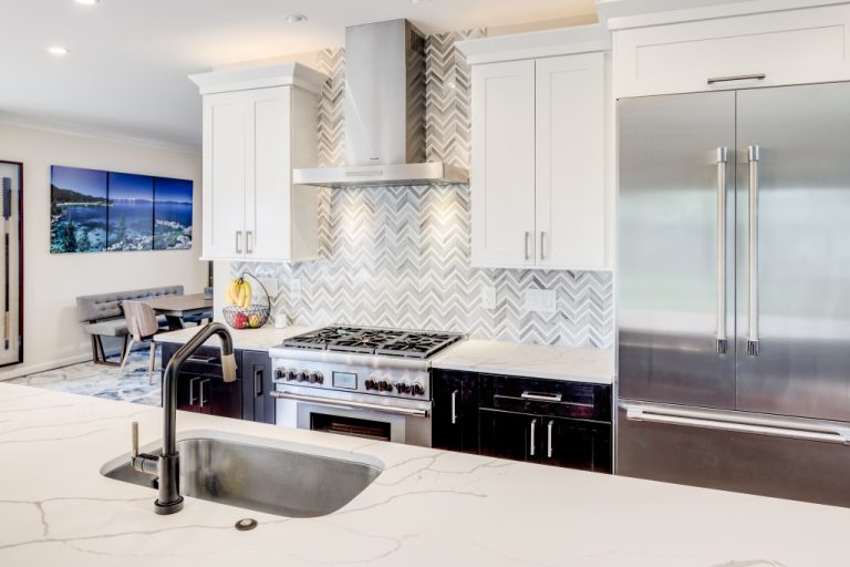 Modern kitchen with white cabinetry, quartz countertops, stainless steel appliances, and herringbone tile backsplash