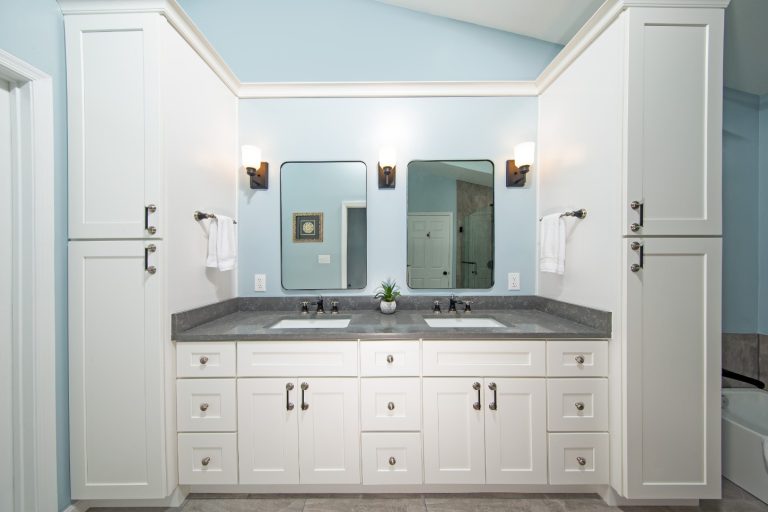 Modern bathroom vanity with dual sinks, white cabinetry, dark countertop, and mirror lighting