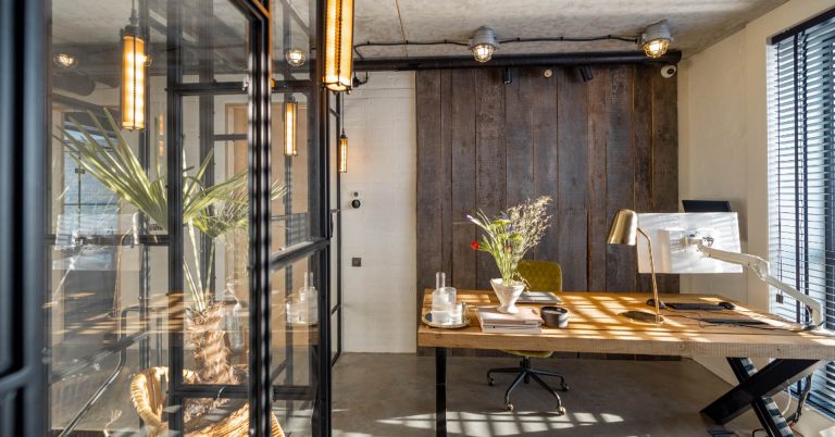 Modern home office with glass partition, wooden desk, and rustic barn door in bright natural light