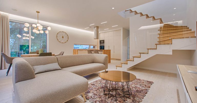 Modern open-concept living room with beige sectional sofa, wooden staircase, and contemporary furnishings