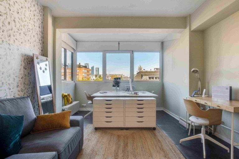 Modern studio apartment with wood flooring, vanity sink, seating area, and city views through large windows