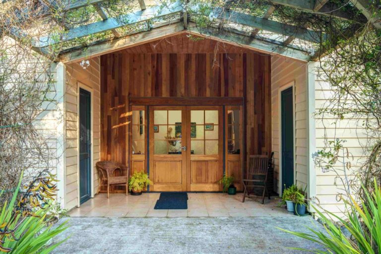 Open wooden garage doors reveal an inviting entrance with warm interior lighting and potted plants flanking the doorway