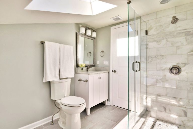 Modern bathroom with white vanity, toilet, marble shower enclosure with glass doors, and chrome fixtures