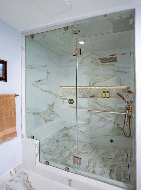 Modern bathroom with marble-patterned glass shower enclosure, gold fixtures, and white subway tile walls