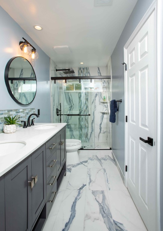 Modern bathroom with gray vanity, marble flooring, walk-in shower with glass enclosure, and round mirror