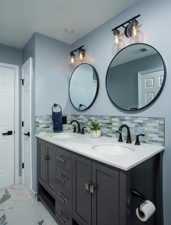 Modern bathroom vanity with dark cabinetry, white countertop, two round mirrors, and chrome fixtures