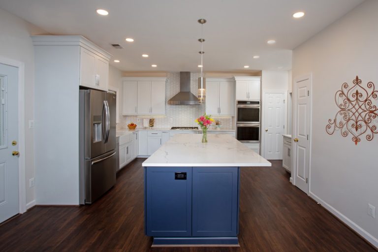 Modern kitchen with white cabinets, blue island, stainless steel appliances and dark hardwood flooring