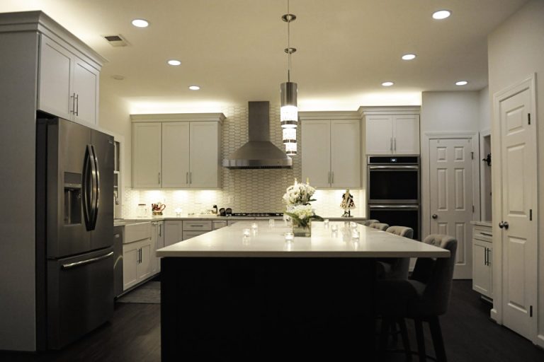 Modern kitchen with white cabinetry, black island, stainless steel appliances, and pendant lighting