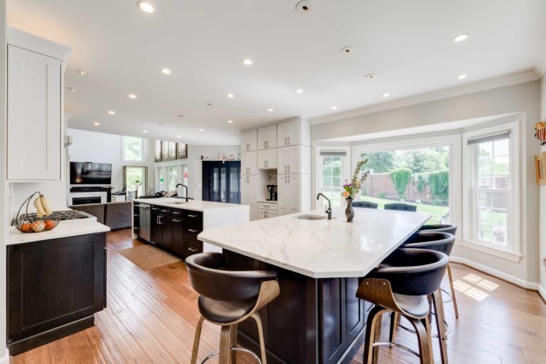 Modern kitchen with white cabinetry, black island, wooden floors, and large windows overlooking the backyard