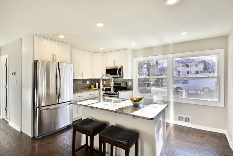 Modern kitchen with white cabinetry, stainless steel appliances, island with seating, and large windows overlooking snowy