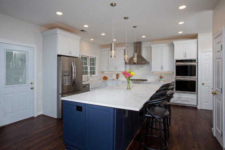 Modern kitchen with white cabinetry, navy blue island, stainless steel appliances, and dark hardwood floors