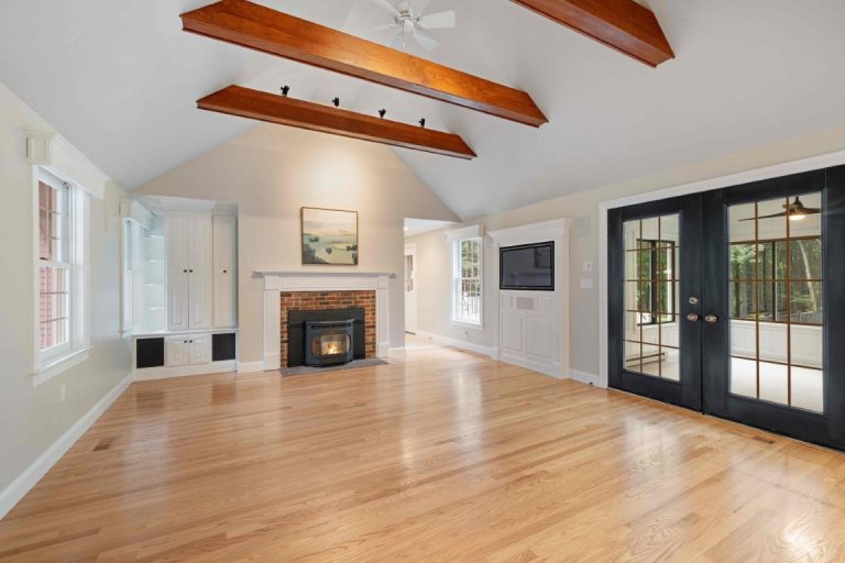 Spacious open-concept living room with wooden beams, fireplace, hardwood floors, and glass doors leading to outdoor space