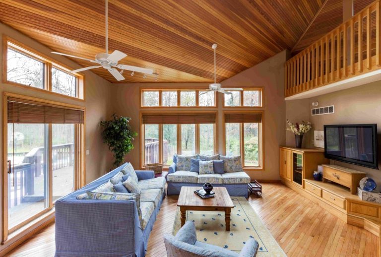 Modern wooden addition living room with blue furniture, exposed beams, and large windows overlooking outdoor space