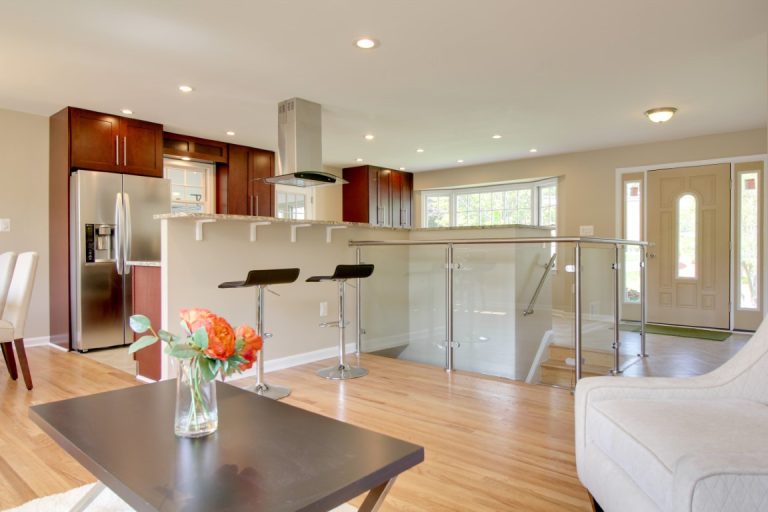 Modern open-concept kitchen with stainless steel appliances, wood cabinetry, island with dark countertop, and hardwood