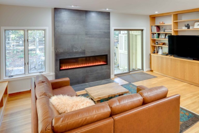 Modern living room with orange leather sofa, fireplace with dark surround, wooden shelving, and hardwood floors