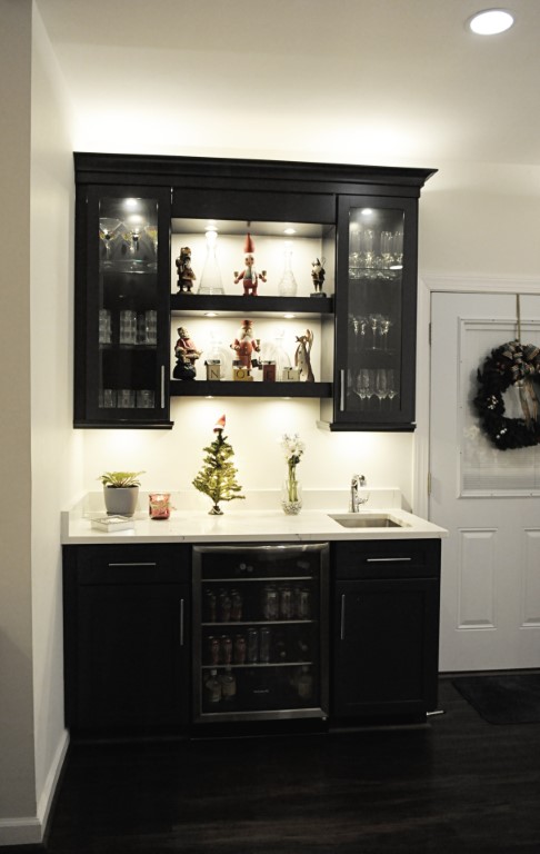 Black kitchen bar cabinet with glass doors, shelving, sink, and decorative dishware display