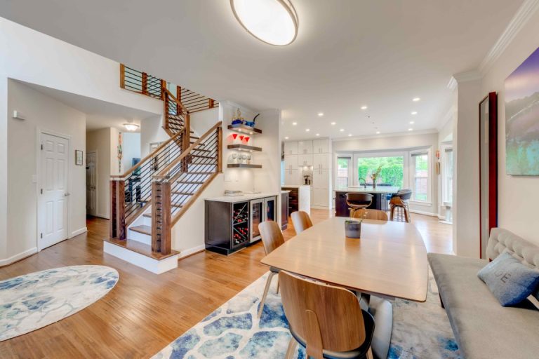 Modern open-concept home interior with wooden dining table, staircase, kitchen, and living areas with hardwood floors