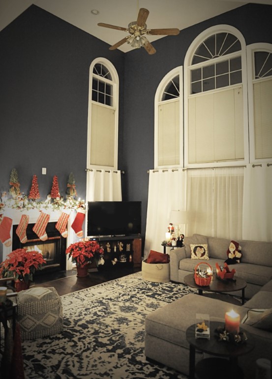 Dark bedroom with cream arched doorways, fireplace mantel decorated with candles and holiday items, ceiling fan, and