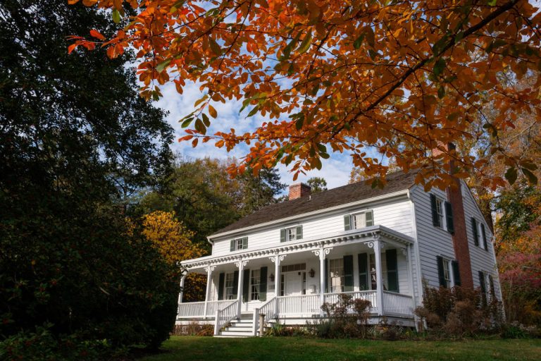 White colonial house with front porch surrounded by autumn foliage and trees